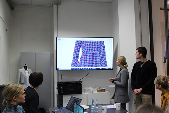 Person präsentiert kariertes Kleidungsstück auf Monitor
