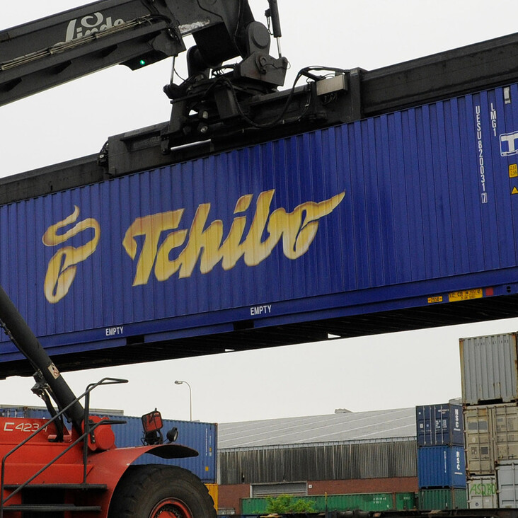 Kran hebt blauen Tchibo-Container im Hafen