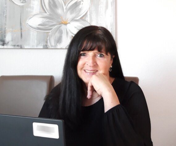 Frau mit Laptop vor Blumenbild, Gesicht verpixelt