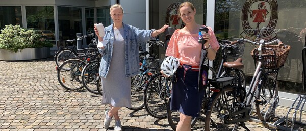 Zwei Frauen mit Fahrrädern und Kaffee vor Bürogebäude