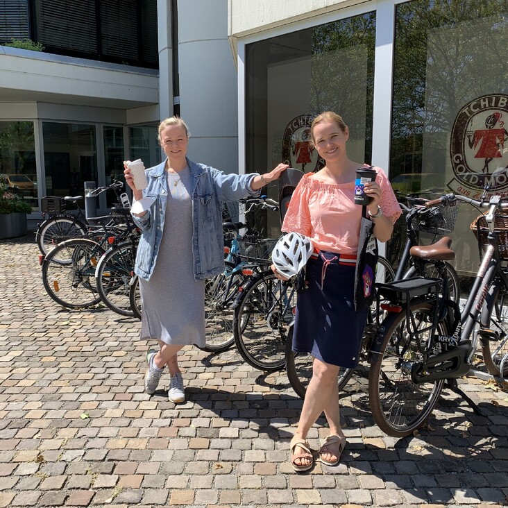 Zwei Frauen mit Fahrrädern und Kaffee vor Bürogebäude