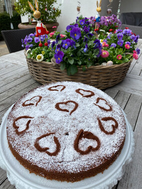 Kuchen mit Puderzucker und Herzmustern vor Blumenkorb