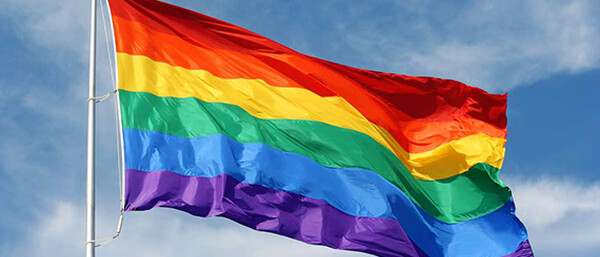 Regenbogenflagge weht vor blauem Himmel