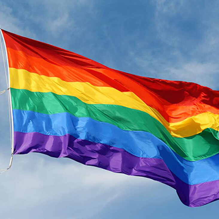 Regenbogenflagge weht vor blauem Himmel