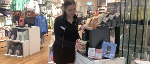 Verkäuferin zapft Kaffee im Bekleidungsgeschäft