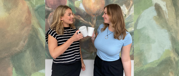 Zwei Frauen stoßen weiße Kaffeetassen an