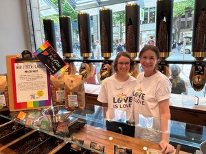 Link: Großansicht des Bildes - Bildinhalt: Café mit Pride-Deko, zwei Personen in Love-is-Love-Shirts
