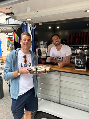Link: Großansicht des Bildes - Bildinhalt: Zwei Männer am Kaffeestand mit Pride-Deko