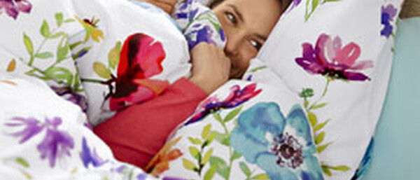 Person im Bett mit bunter Blumenbettwäsche