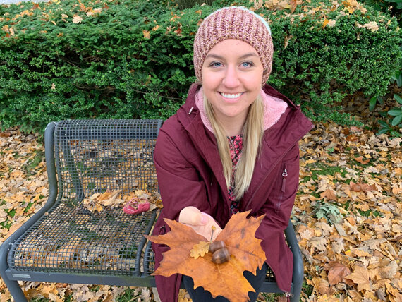 Person auf Parkbank hält Herbstblatt mit Eichel