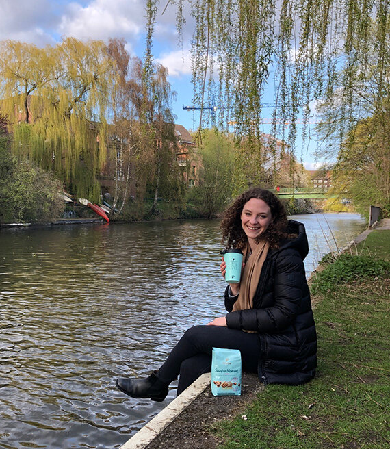 Frau sitzt am Fluss und trinkt aus Becher