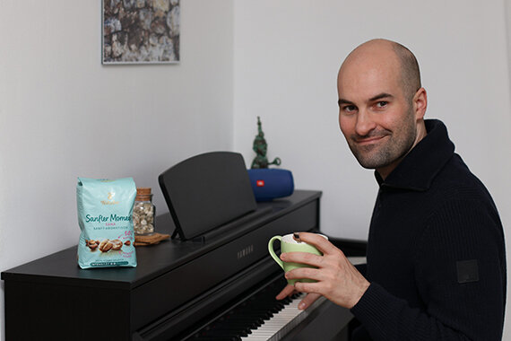 Mann am Klavier mit Tasse und Snacktüte