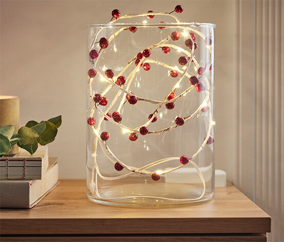 Glasvase mit Lichterkette und roten Beeren