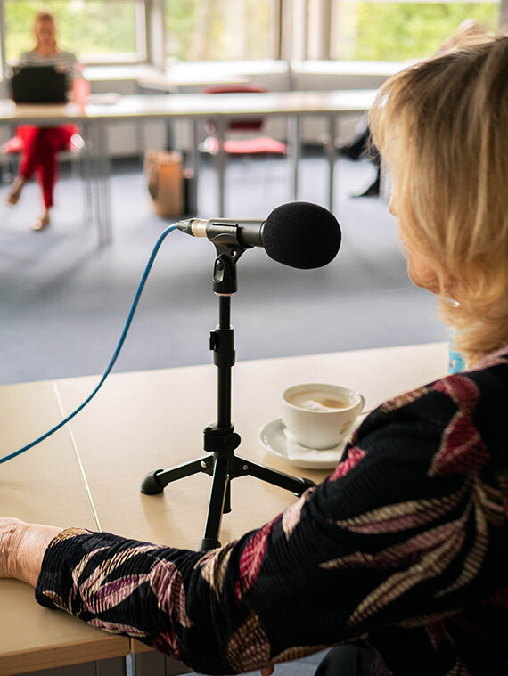 Frau spricht ins Mikrofon, Kaffee auf Tisch
