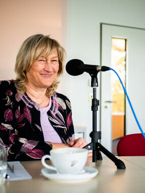 Frau sitzt vor Mikrofon mit Kaffeetasse