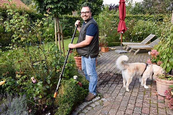 Mann mit Gartengerät und Hund auf Terrasse