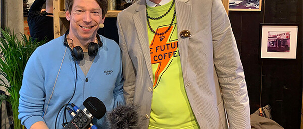 Zwei Personen vor Kaffeemessestand, Schriftzug „FÜNF TASSEN TÄGLICH“