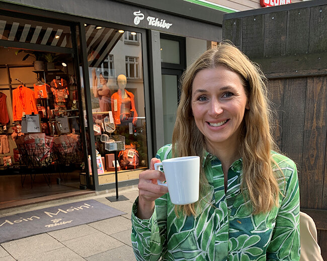 Person mit Kaffeetasse vor Tchibo-Filiale