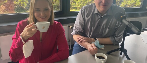 Zwei Personen mit Kaffee und Mikrofon am Tisch
