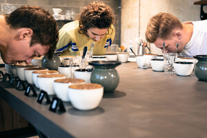 Link: Großansicht des Bildes - Bildinhalt: Menschen riechen an Kaffeeproben auf langer Theke