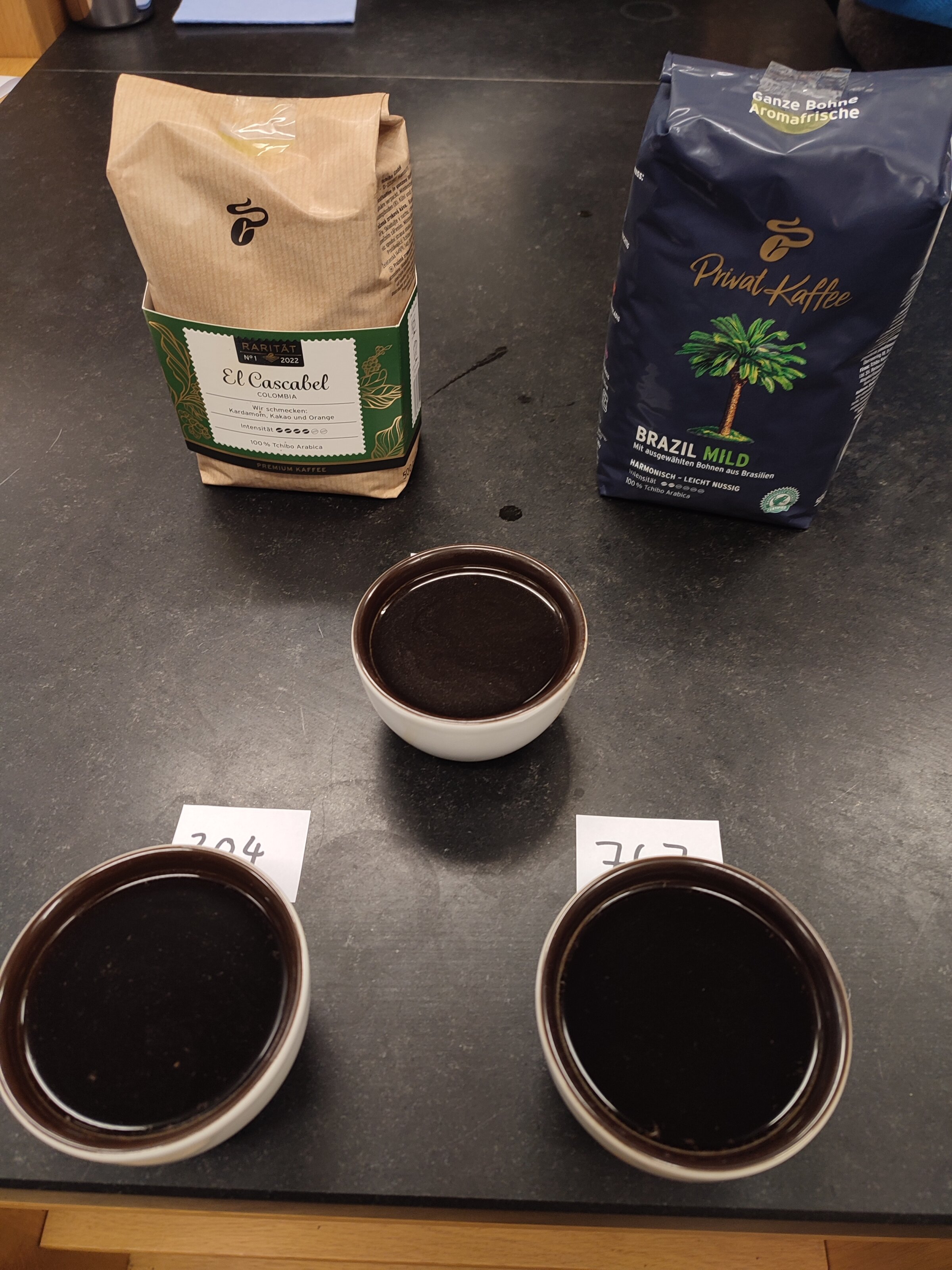 Drei Kaffeetassen vor zwei Kaffeepackungen