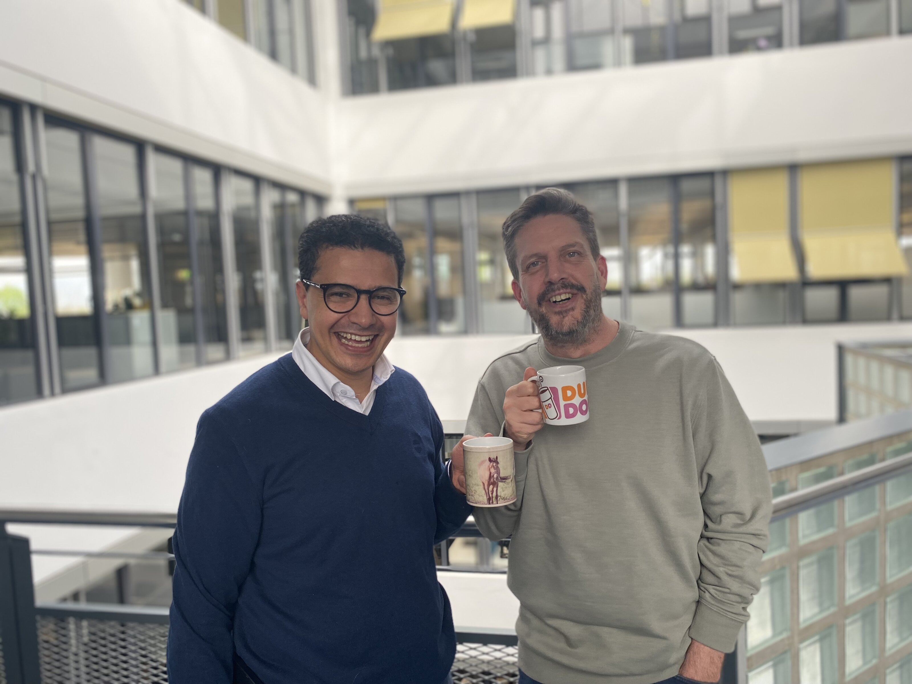 Zwei Kollegen mit Kaffeetassen im Büroflur