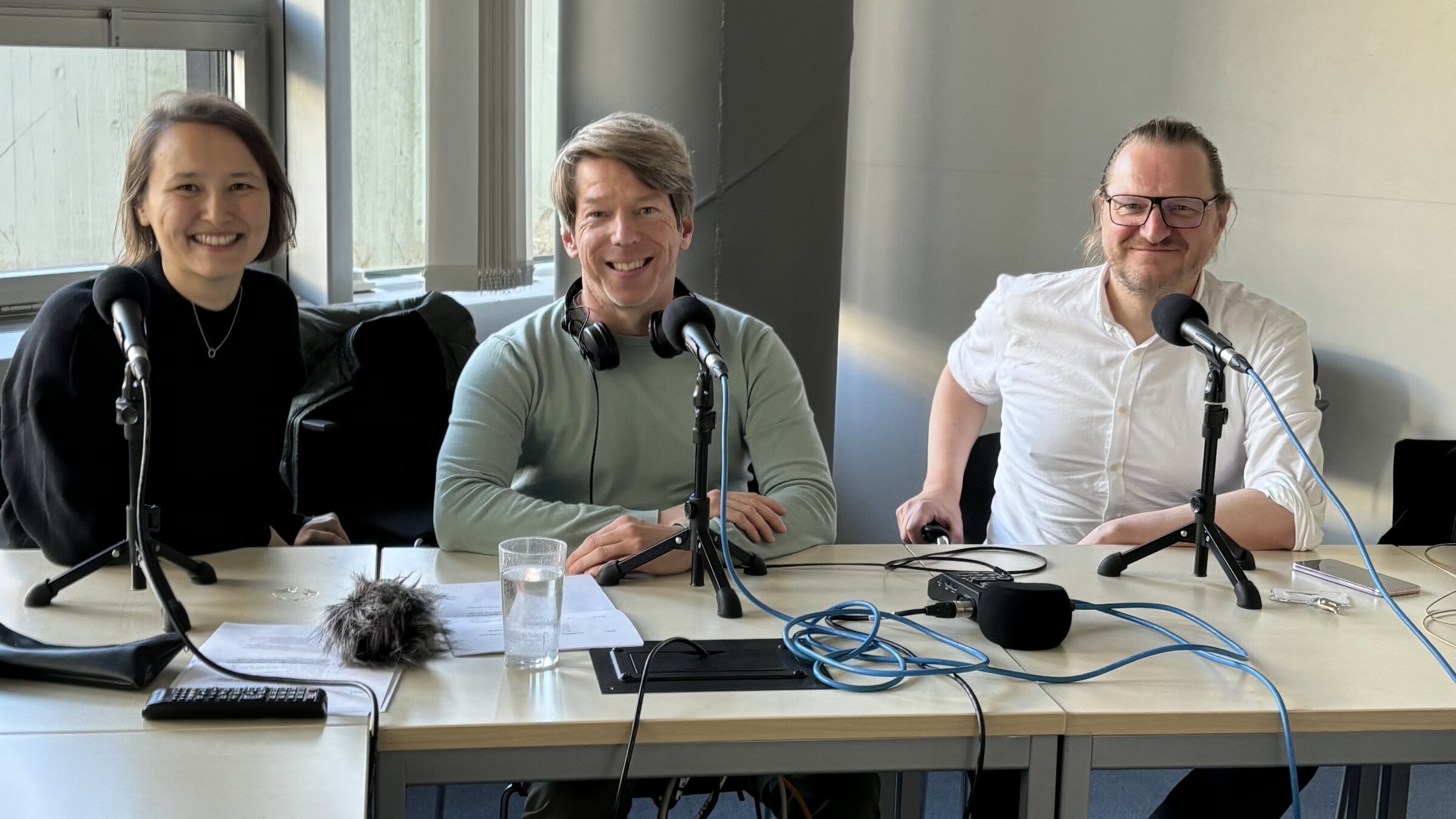 Drei Personen sitzen mit Mikrofonen an einem Tisch