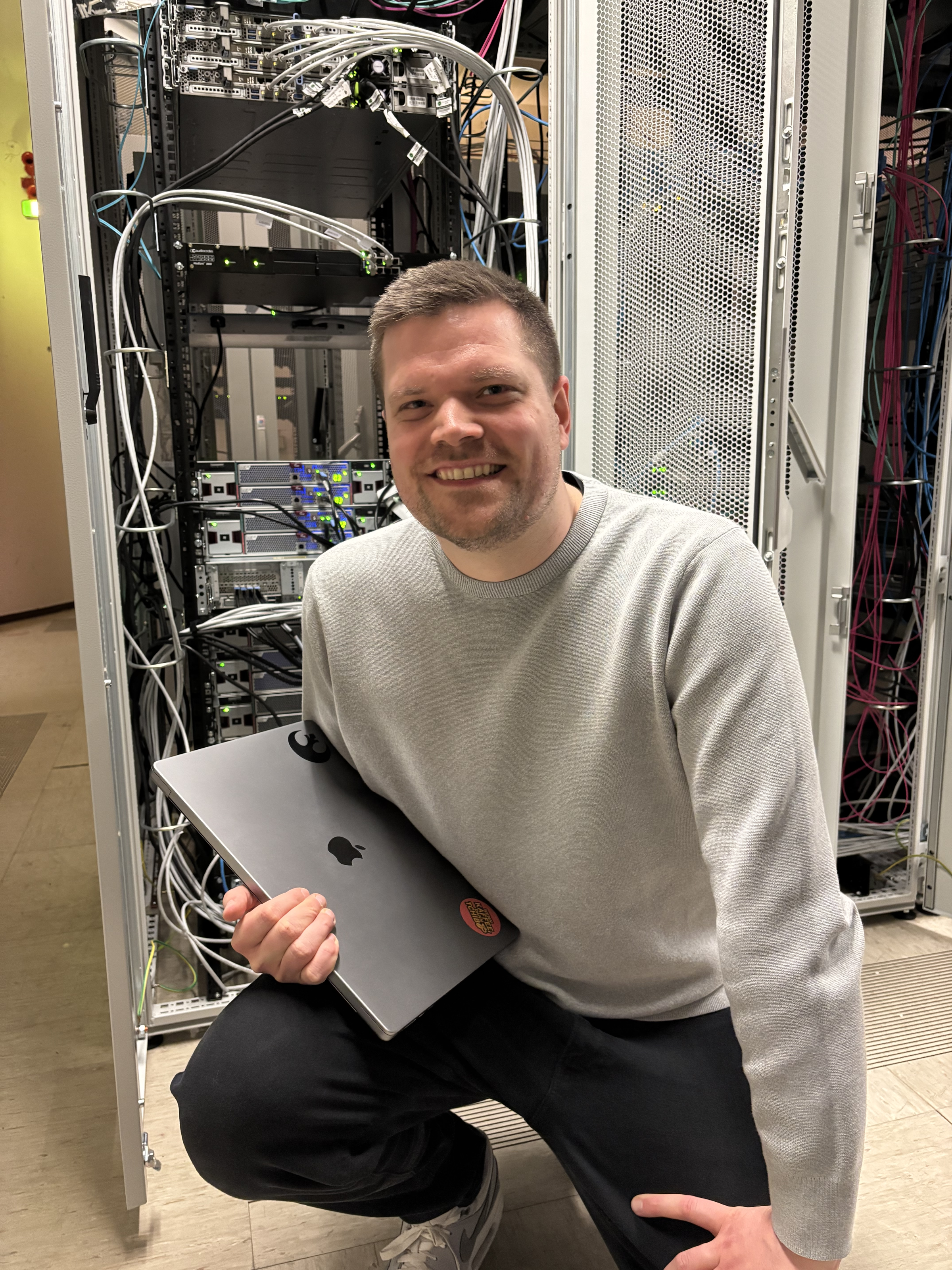 Person mit Laptop kniet vor Serverschrank