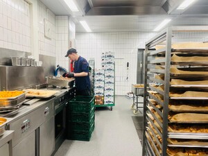 Link: Großansicht des Bildes - Bildinhalt: Mitarbeiter arbeitet in Großküche mit Backblechen