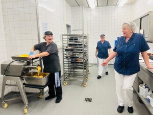 Link: Großansicht des Bildes - Bildinhalt: Küchenpersonal arbeitet an Maschine und Regalen