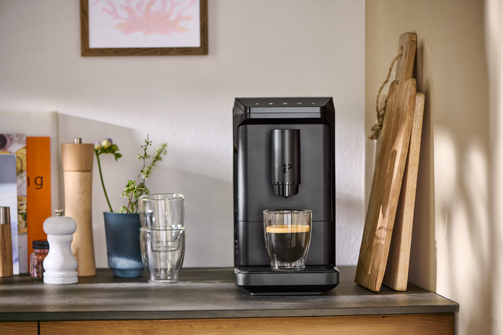 Schwarzer Kaffeeautomat mit Glas Espresso auf Arbeitsplatte