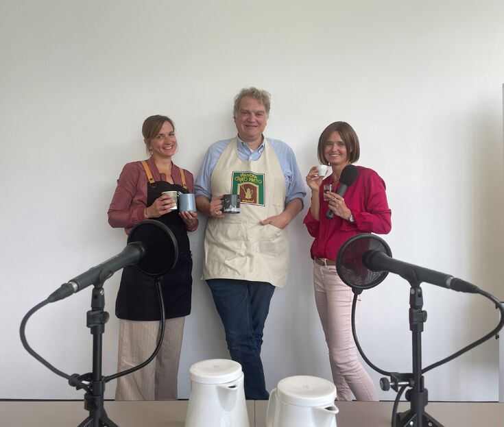 Drei Menschen mit Kaffeetassen vor Mikrofonen
