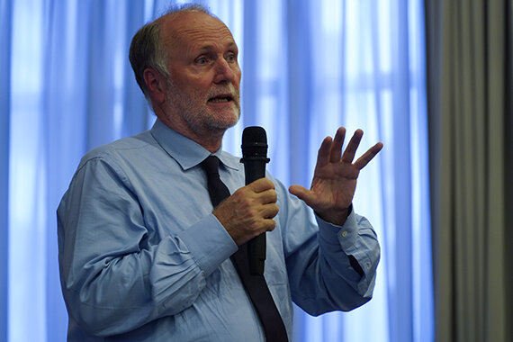 Mann mit Mikrofon spricht vor blauem Vorhang