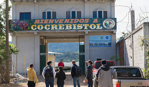 Gruppe vor Tor mit Schild „Bienvenidos a COCREBISTOL“