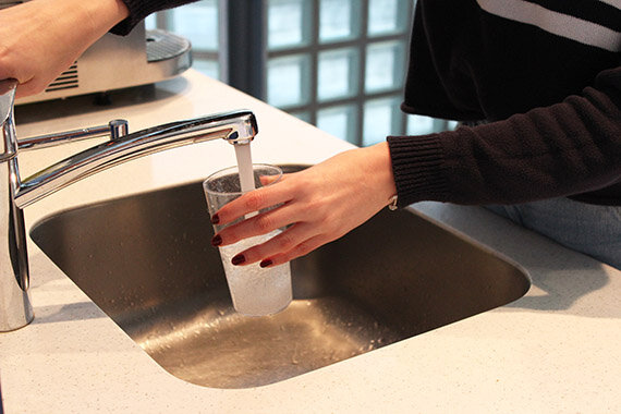 Hand füllt ein Glas mit Wasser am Küchenhahn