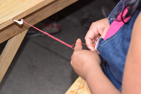 Kind flechtet rotes Band an Holztisch