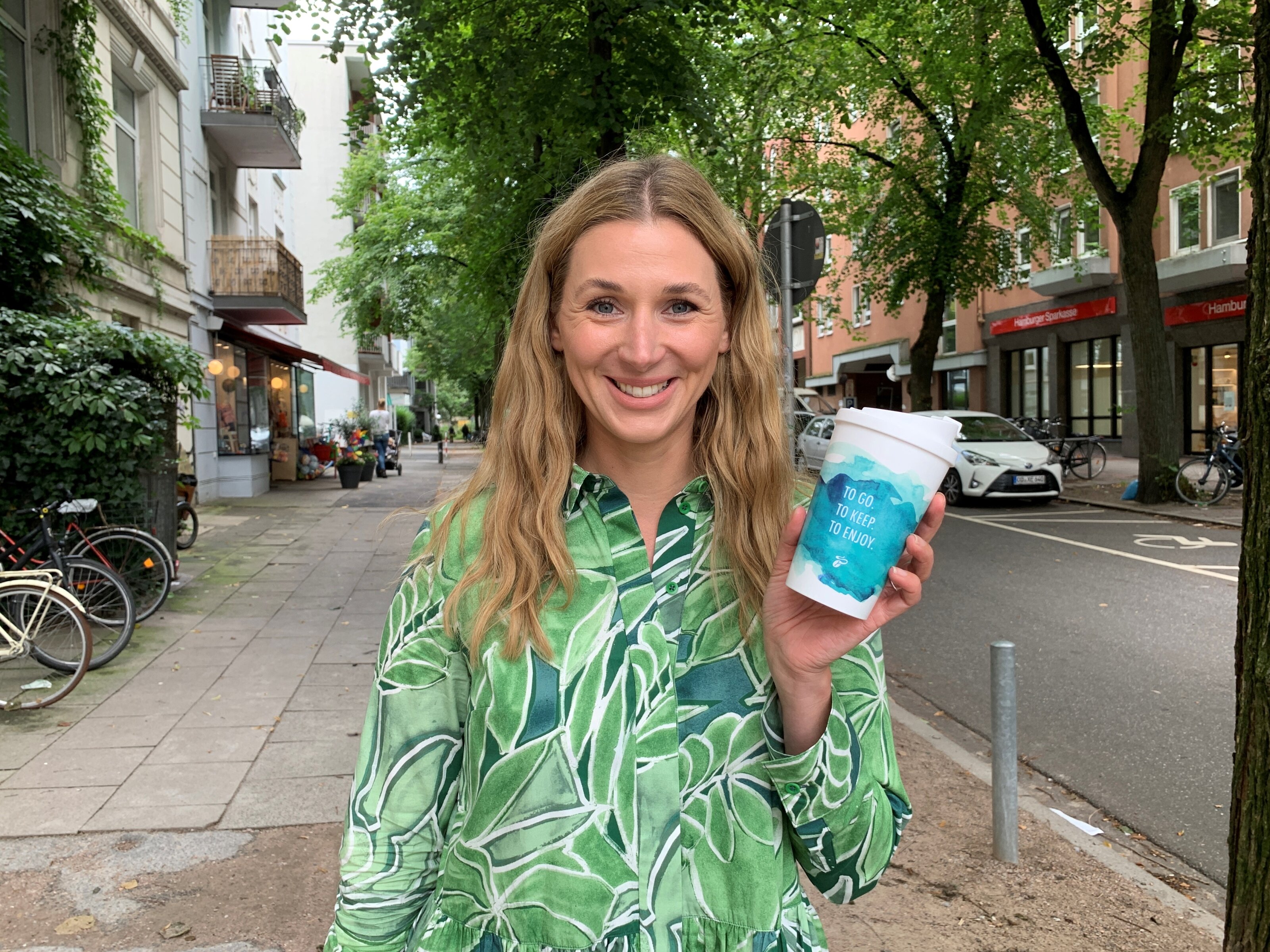 Person mit grünem Hemd hält blauen Kaffeebecher