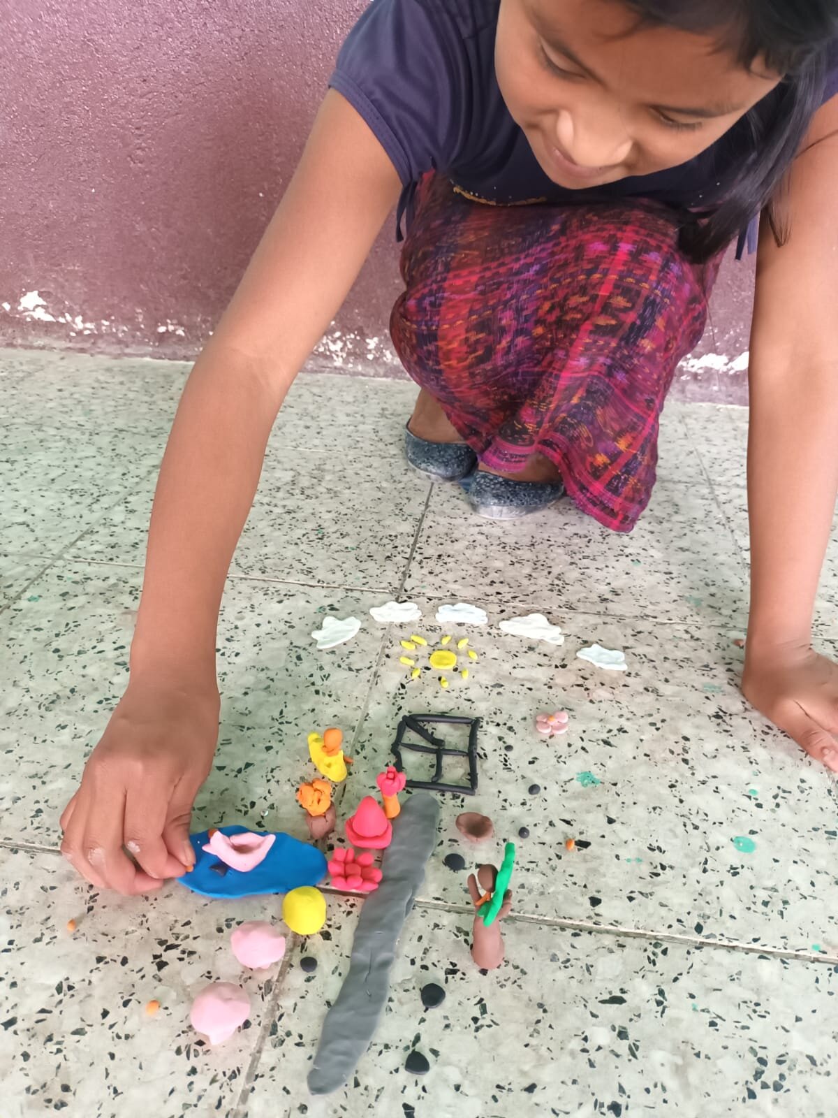 Kind kniet am Boden und spielt mit Knetfiguren
