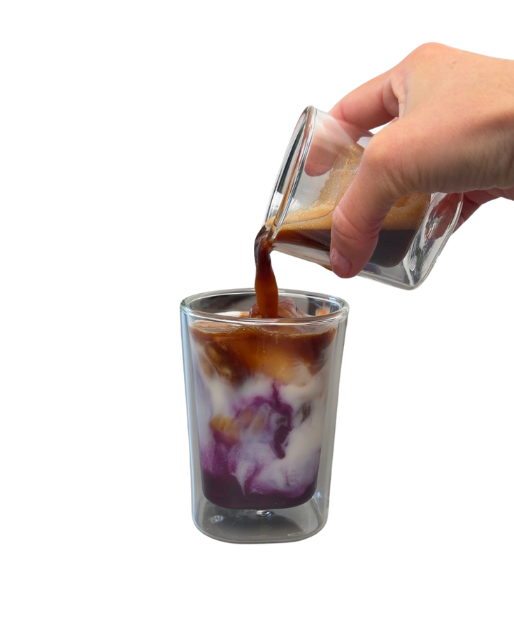 Hand pouring coffee into layered purple latte